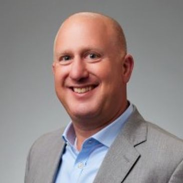 Eric Widhson smiling in a gray suit and blue shirt